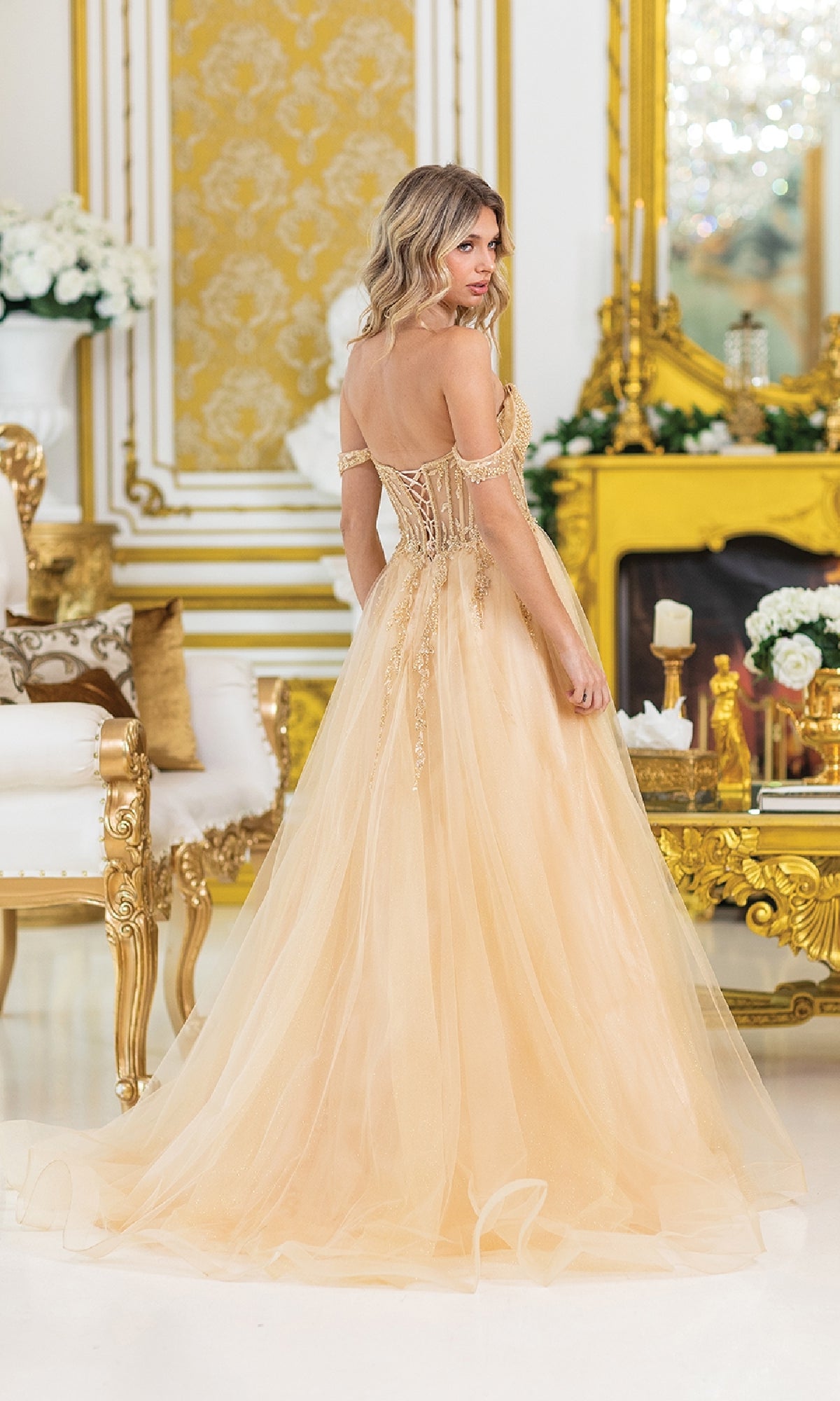 A woman in the Lace-Up Long A-Line Prom Dress: Dancing Queen 4490 poses in a lavish, gold-accented room with ornate furniture and floral decorations.